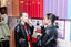 Two women in black leather jackets apply makeup at a colorful station with red, orange, and purple panels in the background.